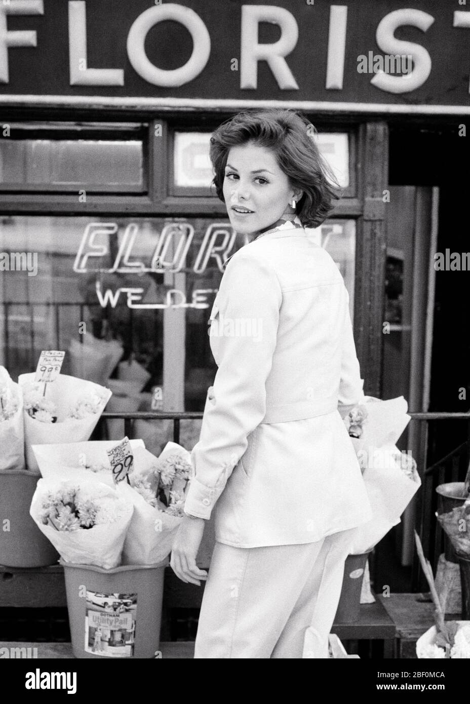 1970 JOLIE TÊTE DE FEMME BRUNETTE TOURNÉE SUR L'ÉPAULE REGARDANT LA CAMÉRA DEBOUT DEVANT LE FLEURISTE MAGASIN BOUQUETS DE TROTTOIR - F13601 HAR001 HARS JOLIE VENTE SERVICE À LA CLIENTÈLE PROFESSIONS TRANSFORMÉES PETITE ENTREPRISE STOREFRONT ÉLÉGANT FLEURISTE MOYENNE ADULTE FEMME PANTALON POUR FEMME DE MILIEU D'ADULTE S'ADAPTE À LA JEUNE FEMME ADULTE NOIR ET BLANC CAUCASIEN ETHNICITÉ HAR001 À L'ANCIENNE Banque D'Images