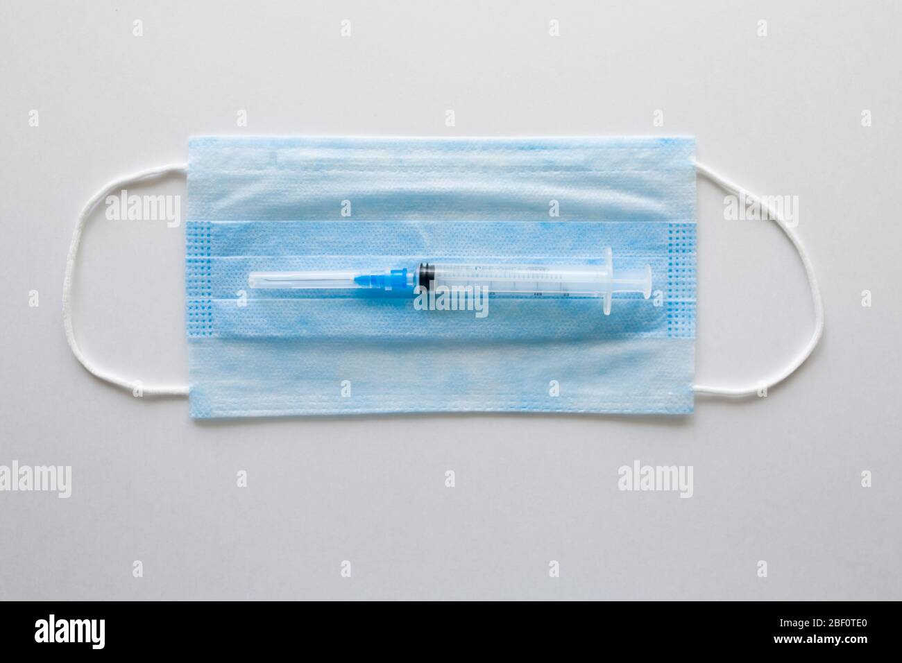 Masque médical antiviral pour la protection contre COVID-19. Bandage respiratoire médical visage sur fond blanc avec seringue. Banque D'Images