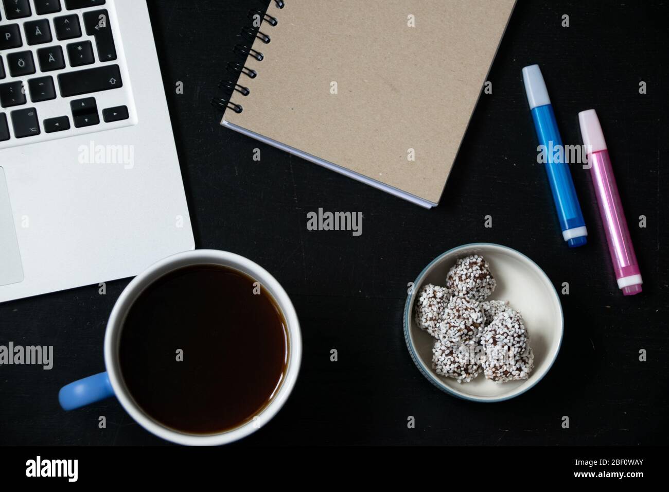 Vue depuis le dessus du lieu de travail moderne avec tasse de thé, ordinateur portable, stylos, carnet et pâtisserie traditionnelle suédoise de pause café - boules de chocolat Banque D'Images