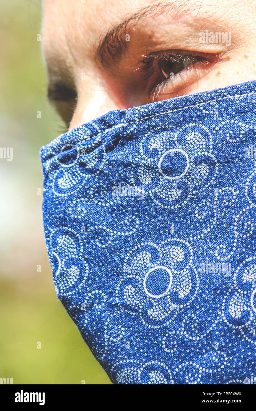 Jeune femme caucasienne à l'extérieur avec un masque de visage en tissu bleu pendant la pandémie de coronavirus. Coronavirus, éclosion de COVID-19. Concept de protection antivirus. Arrière-plan flou. Photo verticale. Banque D'Images