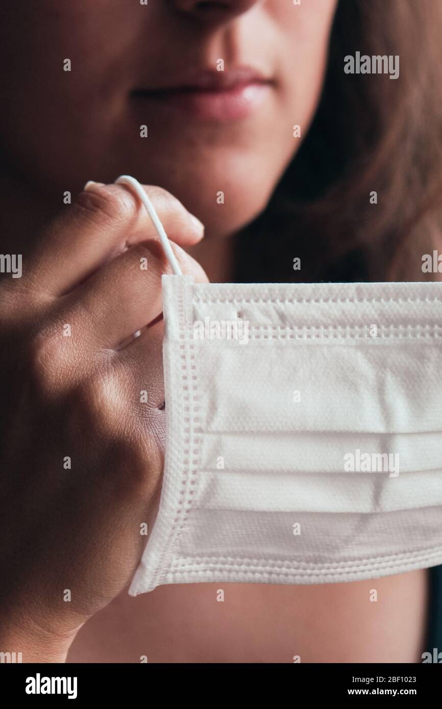 Photo détaillée d'une femme blanche non reconnaissable mettant sur un masque médical blanc pour prévenir l'infection. Fond flou, foyer sur le masque. Coronavirus, COVID-19 quarantaine. Concept de verrouillage. Banque D'Images