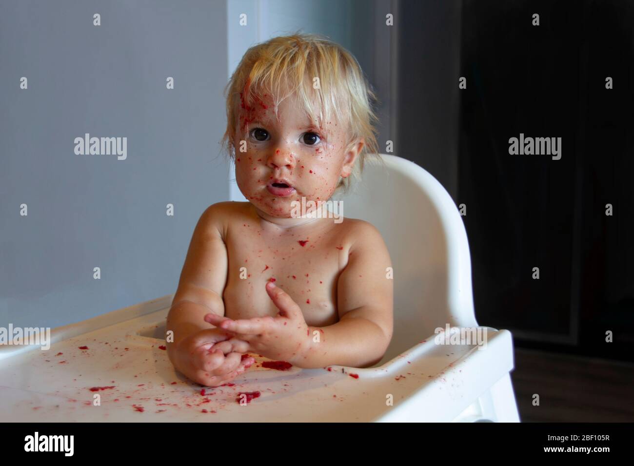 Bébé caucasien enfant avec des yeux bruns foncés assis sur la chaise haute après avoir mangé de la nourriture Banque D'Images