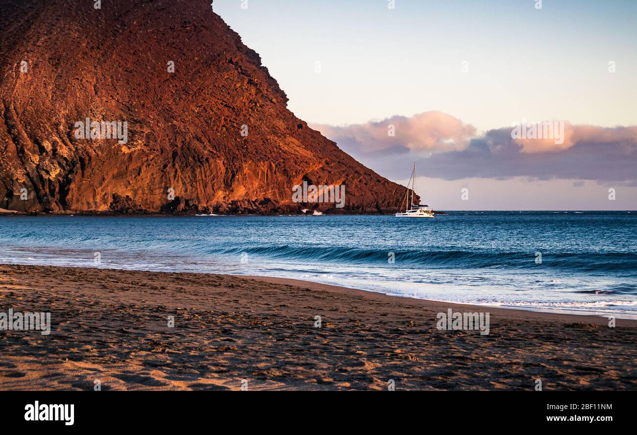 Coucher de soleil sur la plage de la Tejita avec un yacht amarré près de la légendaire 'colline Rouge' (la Montaña Roja) dans le sud de Ténérife, îles Canaries, Espagne. Banque D'Images