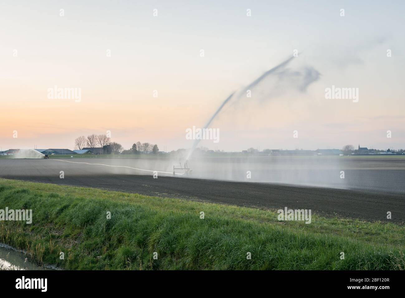 Les agriculteurs irriguent un champ labouré et semé en Hollande avec un système sprinkleur au coucher du soleil Banque D'Images