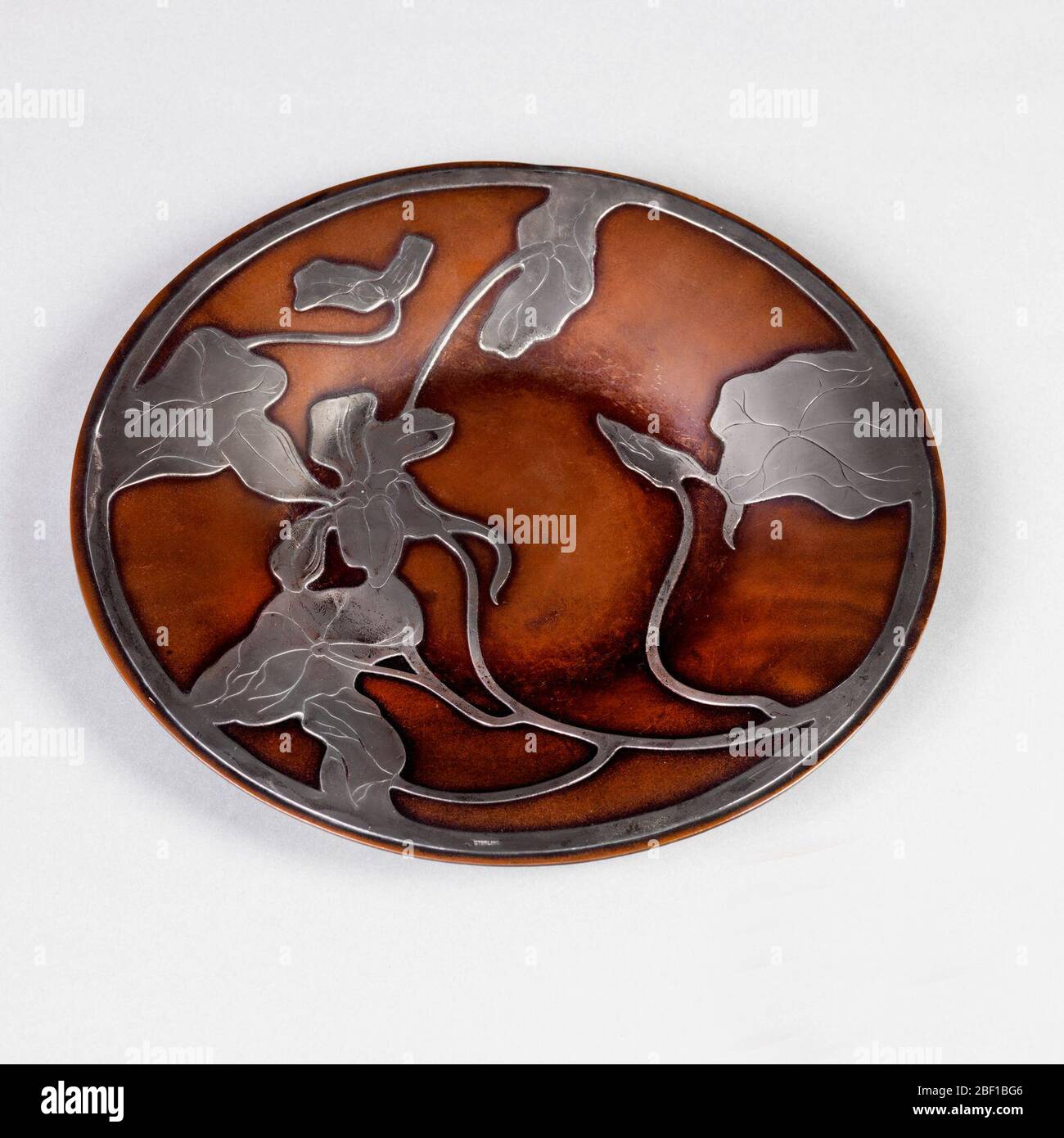 Plaque. Plaque circulaire en cuivre avec motif superposé en argent de feuilles, vignes et fleurs. Banque D'Images