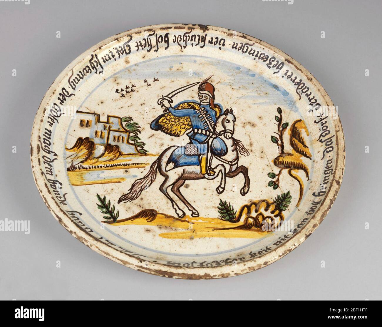 Plaque. Plat représentant un soldat tenant un sabre à cheval dans un paysage avec bâtiment en arrière-plan gauche. Bordure inscrite en texte noir. Banque D'Images