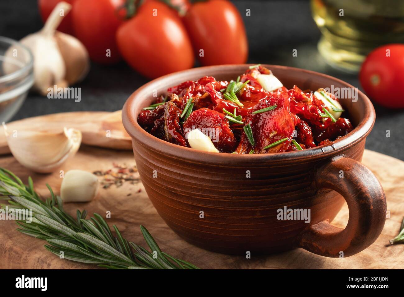 Tomates séchées au soleil avec ail, romarin et épices dans un bol en argile sur un tableau de découpe en bois d'olive. Banque D'Images