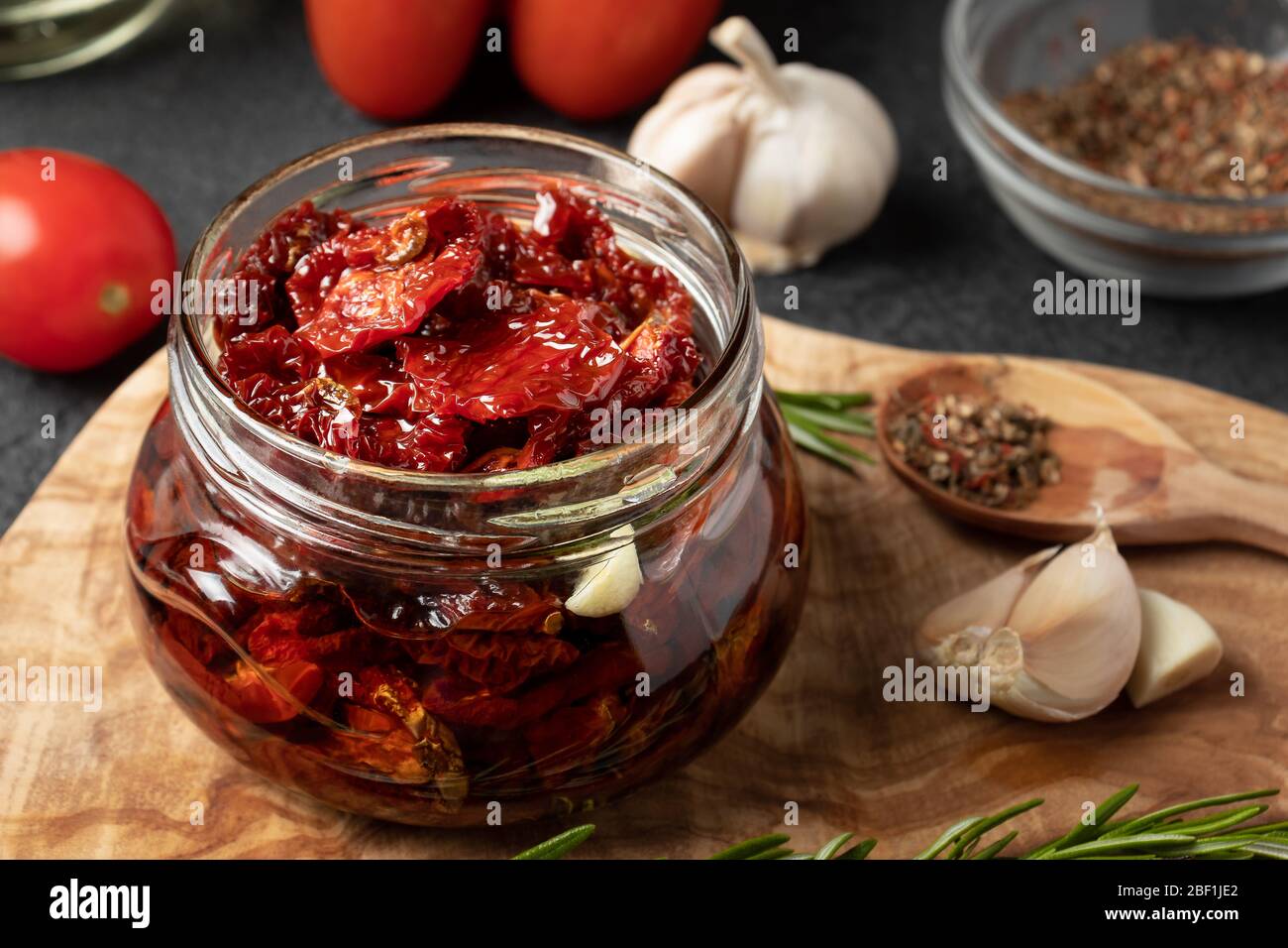 Tomates séchées au soleil avec ail, romarin et épices dans un pot en verre sur un tableau de découpe en bois d'olive. Banque D'Images