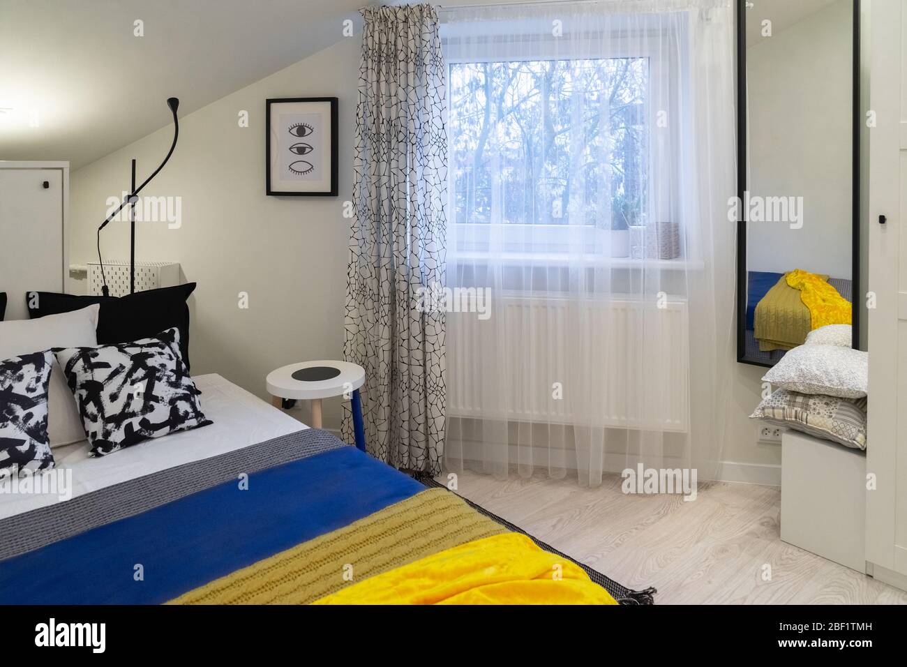 Partie d'une petite chambre confortable récemment meublée dans le grenier d'une ancienne maison. Principalement blanc et noir avec un accent de couvre-lits bleus et jaunes. Banque D'Images