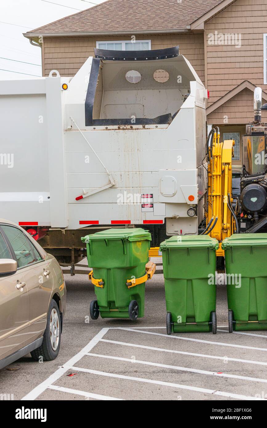 Tir vertical d'un camion à ordures avec un bras de robot attrapant un conteneur à ordures en préparation pour le vider dans le camion à ordures. Banque D'Images