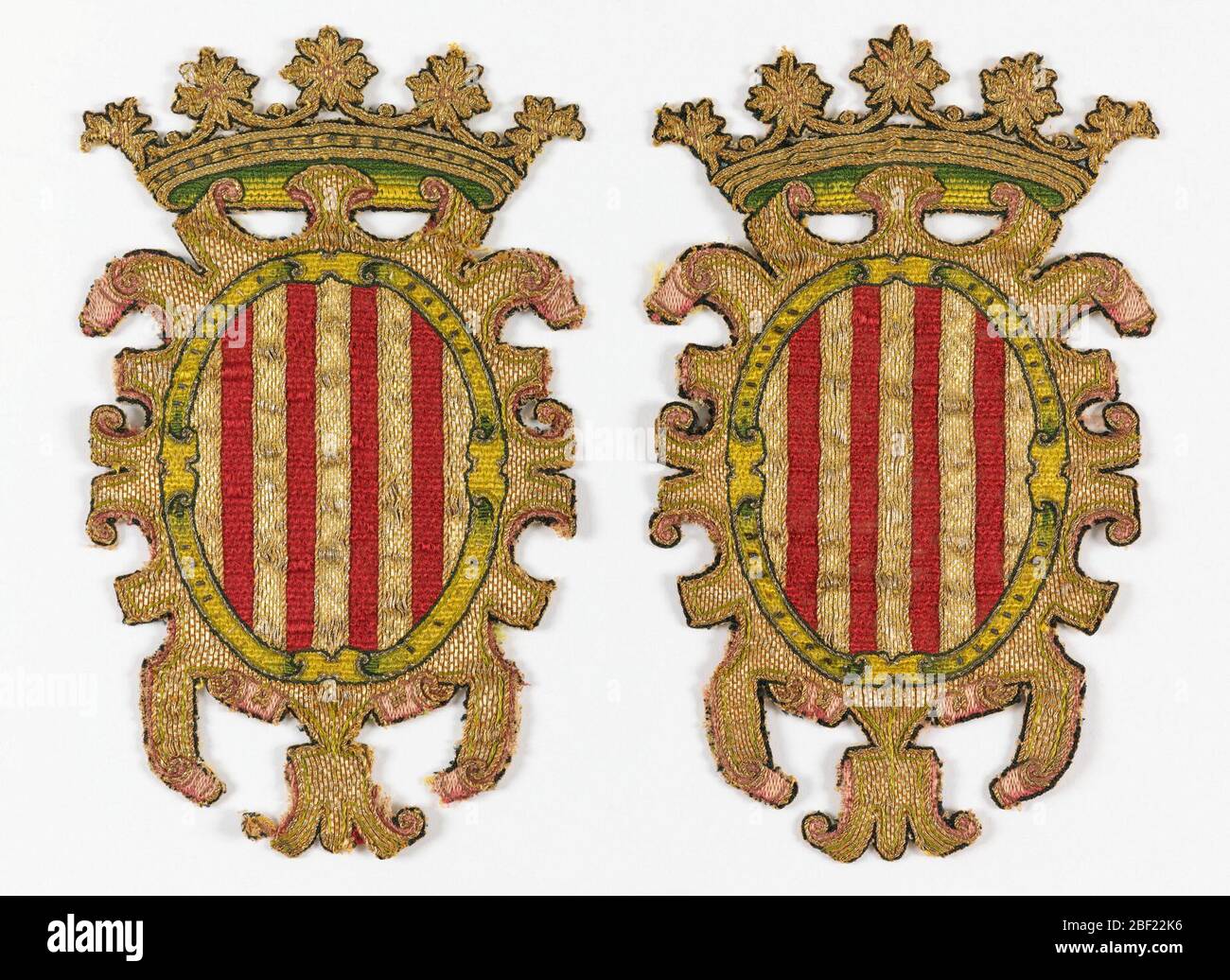 Éboucheon. Bouclier ovale avec rayures verticales rouges et or entourées d'un manteau arabesqué or, recouvert d'une couronne avec rosettes sur le dessus. Détails de la couture en satin vert et rose ombré ; contours noirs. Banque D'Images