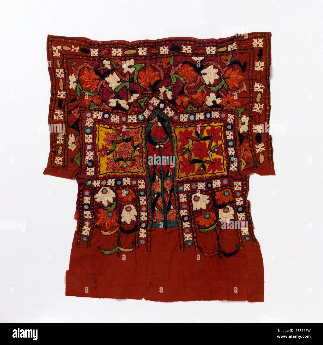 Fragment. Tissu en soie rouge piecté de coton rouge, jaune et bleu et brodé avec un motif de fleurs stylisées et de bordures étroites. Banque D'Images