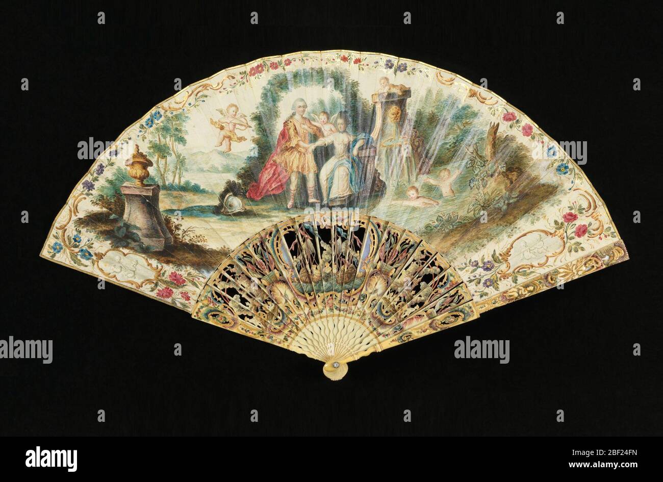 Ventilateur plissé. Ventilateur plissé avec feuille de papier peint. Le montage obverse montre un couple – la femme est assise, et l'homme se tient sous un arbre par une fontaine avec deux coupides de bain. Un cupid est de prendre une flèche au couple. Banque D'Images