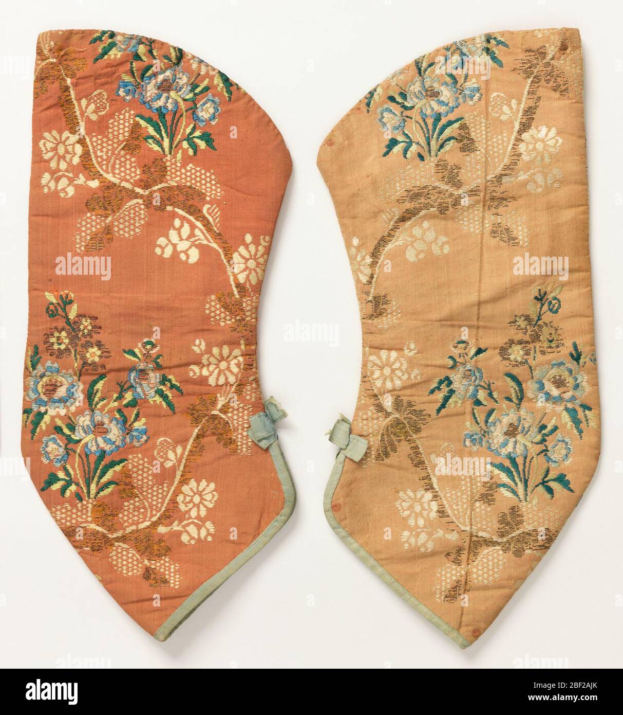 Paire de manches. Paire de manches qui auraient été attachées à une robe du XVIIIe siècle. Manche gauche mal délavé. Terre de couleur corail avec une vigne à courbes avec des fleurs bleues et blanches. Finition en bas avec reliure bleue et petit noeud. Banque D'Images