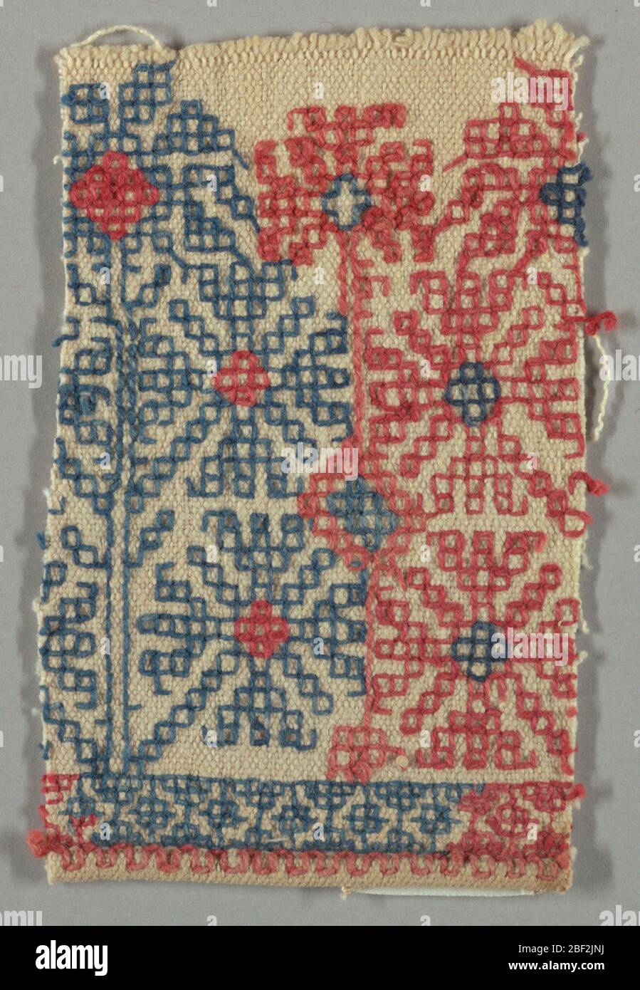 Textile. La conception de quatre fleurs stylisées disposées autour d'un bloc central, travaillée en rouge et bleu sur un sol blanc. Banque D'Images