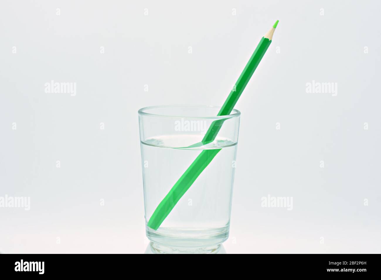 Crayon jaune et vert, à l'intérieur d'un verre rempli d'eau, explication de réfraction de lumière Banque D'Images