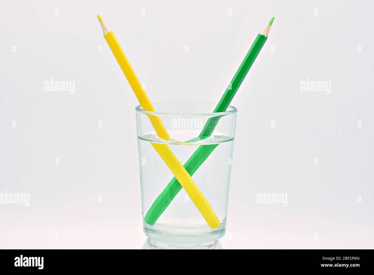 Crayons jaunes, bleus et verts, à l'intérieur d'un verre rempli d'eau, explication réfraction de la lumière Banque D'Images