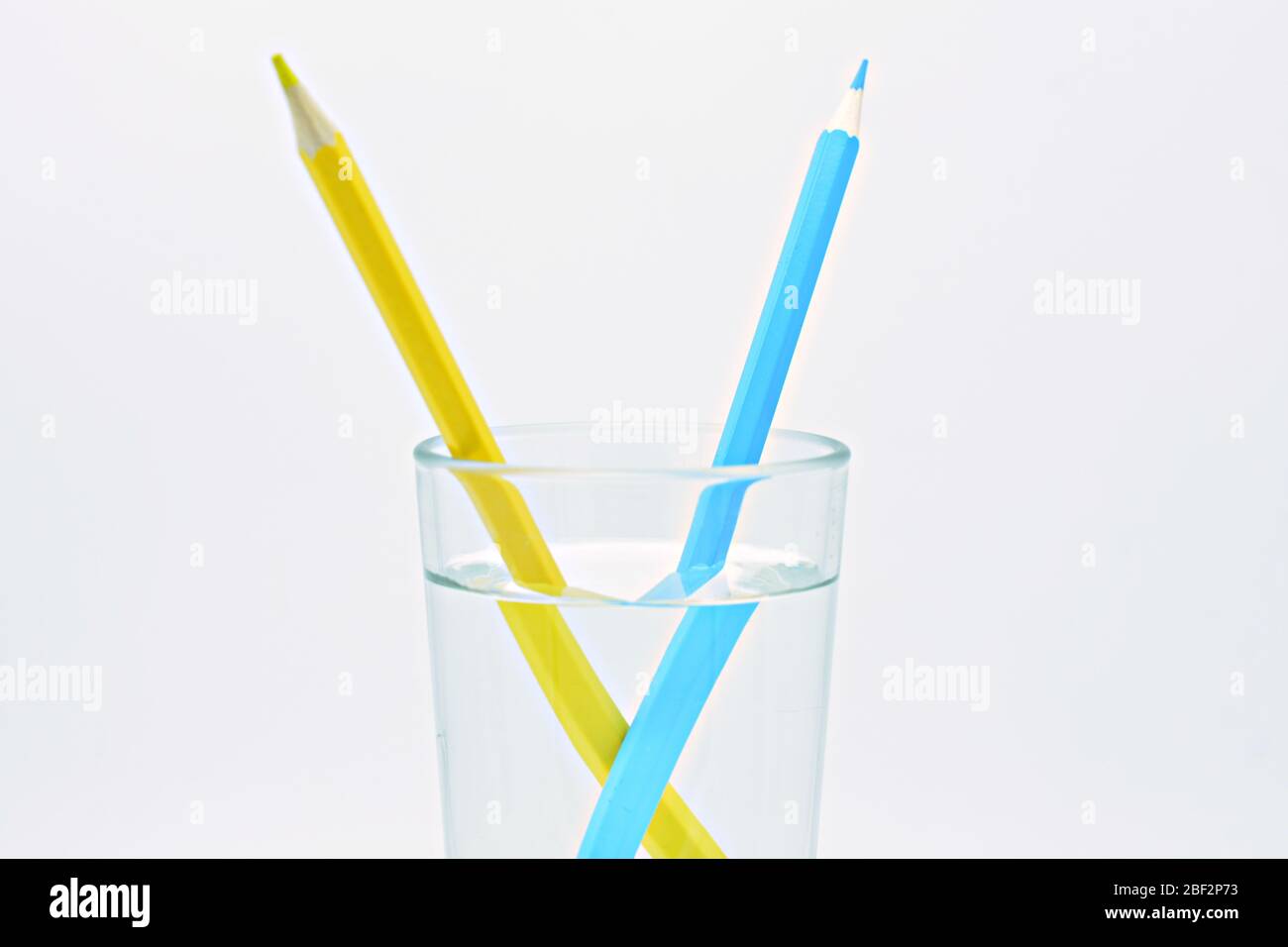 Crayons jaunes, bleus et verts, à l'intérieur d'un verre rempli d'eau, explication réfraction de la lumière Banque D'Images