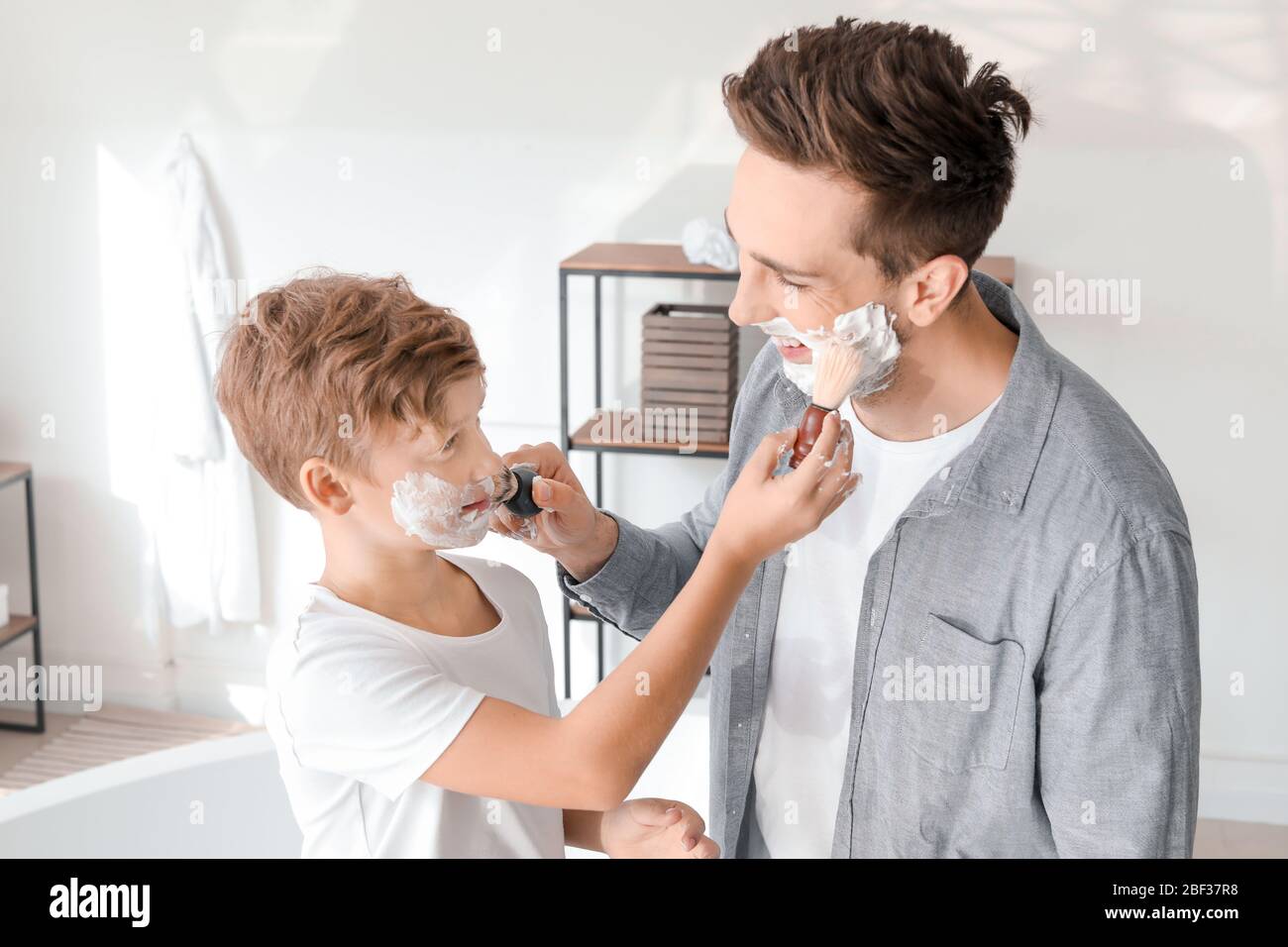 Père avec fils appliquant de la mousse de rasage sur leurs visages dans la salle de bains Banque D'Images