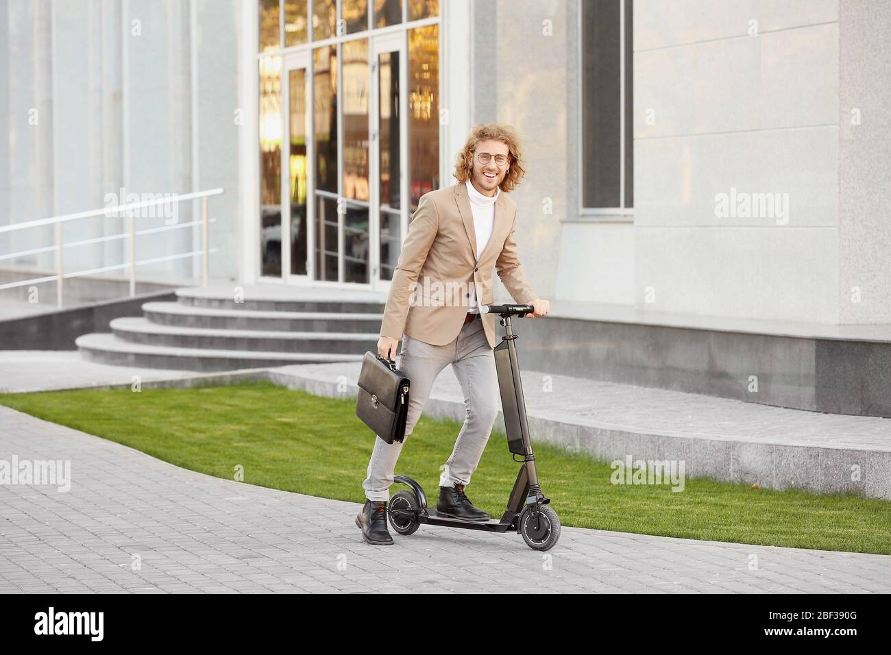 Jeune homme d'affaires avec scooter de coup d'enfant à l'extérieur Banque D'Images