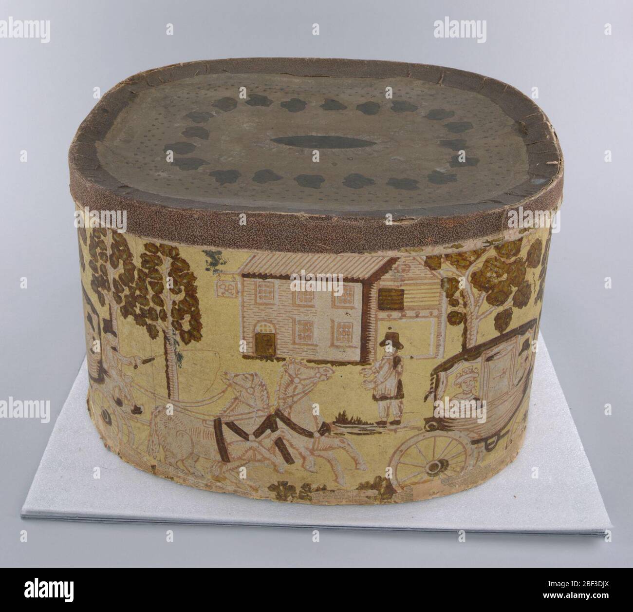 Boîte à bande et couvercle. Transport ferroviaire; autocar dessiné par les chevaux; arrière-plan de taverne ou auberge. Rouge et vert sur le champ jaune. Couverture : médaillon de même couleur de feuilles de raisin et effet de dentelle à la frontière. Banque D'Images