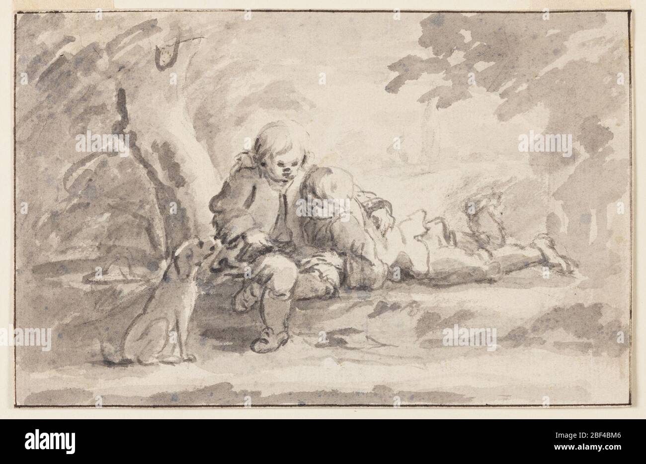 Deux garçons regardant un livre. Un garçon est assis sous un arbre avec un livre dans ses genoux, son bras autour des épaules de l'autre garçon. L'autre garçon est allongé sur son estomac, appuyé sur ses coudes. Un chien est expectantly à gauche du garçon assis. Banque D'Images