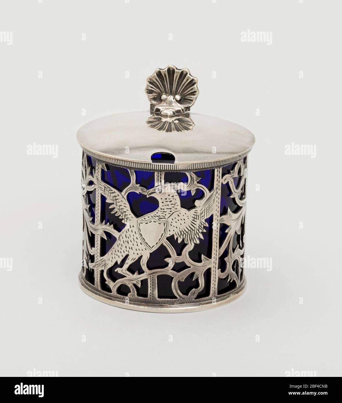Pot à moutarde. Cage cylindrique (A) avec animaux et oiseaux parmi les rouleaux feuillus, en argent découpés. Poignée de sangle, plate sur le dessus. Couvercle à charnière avec repose-pouce et orifice pour cuillère. Insert cylindrique en verre bleu foncé (b). Banque D'Images