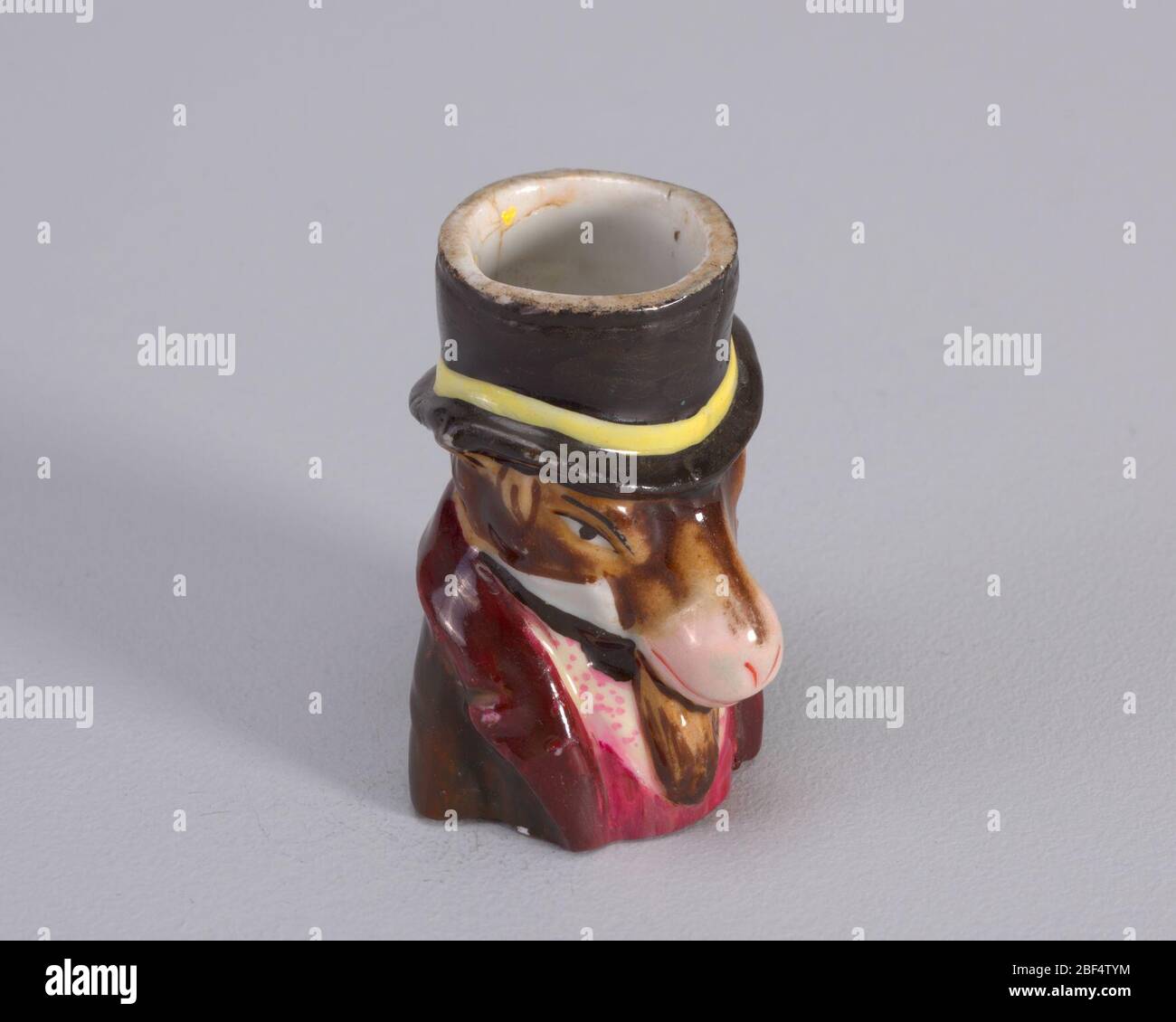 compatibilité. Figure de chapeau de tête d'âne avec bande jaune. La figure porte également un manteau bordeaux avec un gilet magenta et une chemise blanche avec des points magenta. Banque D'Images