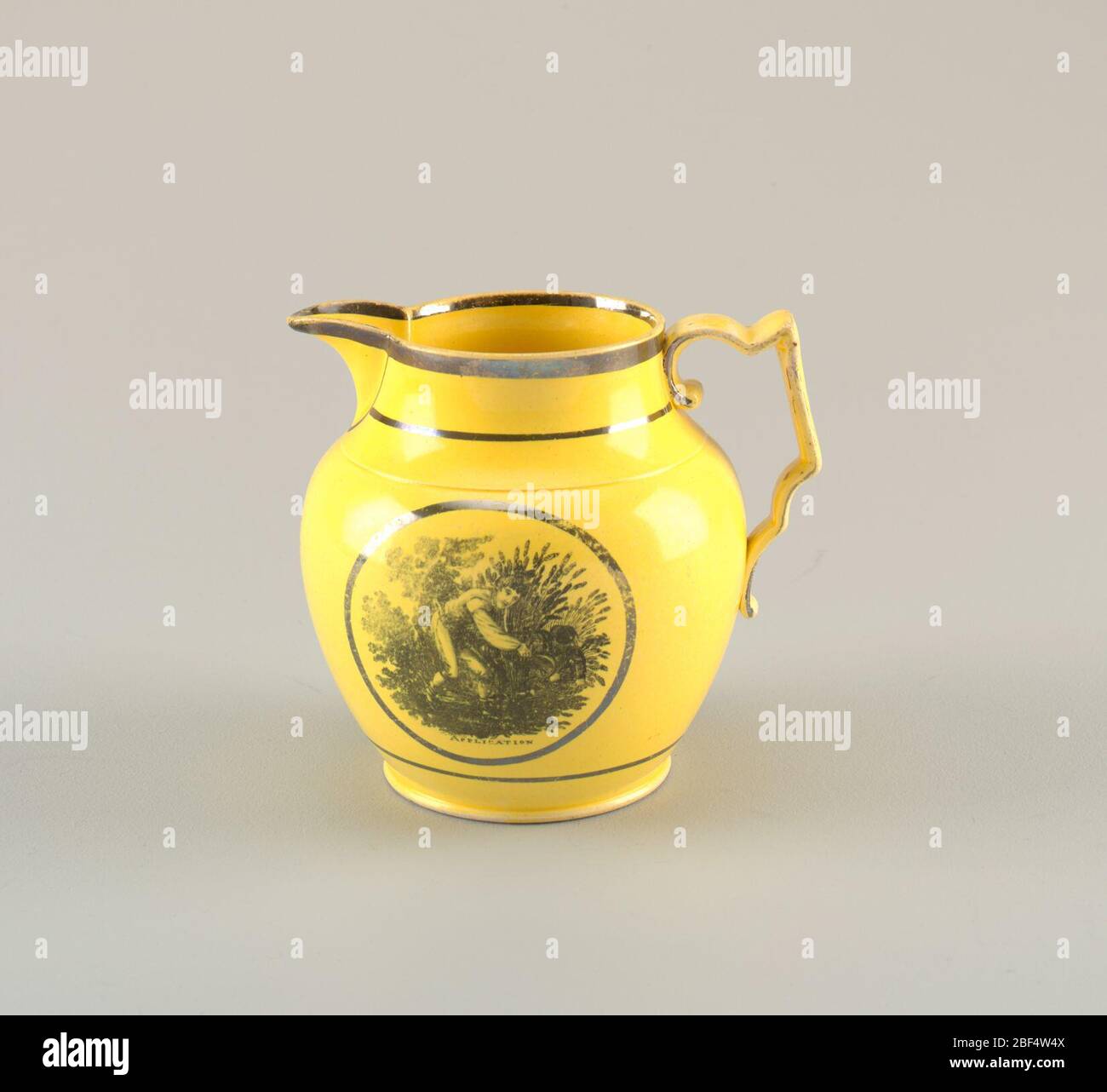 Pichet. Pichet bulbe en jaune avec bec pointu et poignée angulaire et courbée. Bordure noire sur la jante et la base. La représente le jeune homme qui récolte du blé dans un cadre circulaire. Ci-dessous, inscrit : "DEMANDE". Banque D'Images