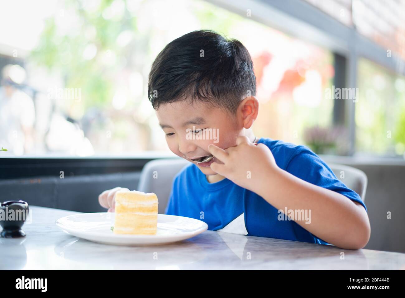 Cute little Asian boy eating cake dans une boulangerie ou un café. Banque D'Images