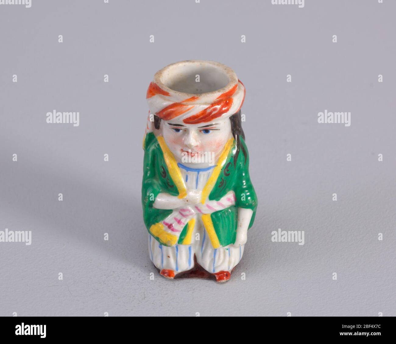 compatibilité. Figure de l'homme portant un costume proche de l'est avec une veste verte avec col jaune et attaché avec ceinture blanche et rayures rouges et tenue blanche sous avec des rayures bleu clair. La figure porte du turban blanc avec des rayures diagonales. Banque D'Images