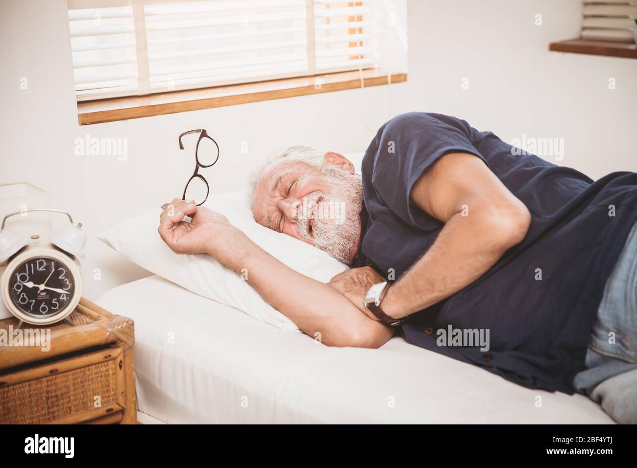 Un aîné se sentant confortable se poser sur le lit, vous pouvez dormir ou vous réveiller le matin en bonne santé Banque D'Images