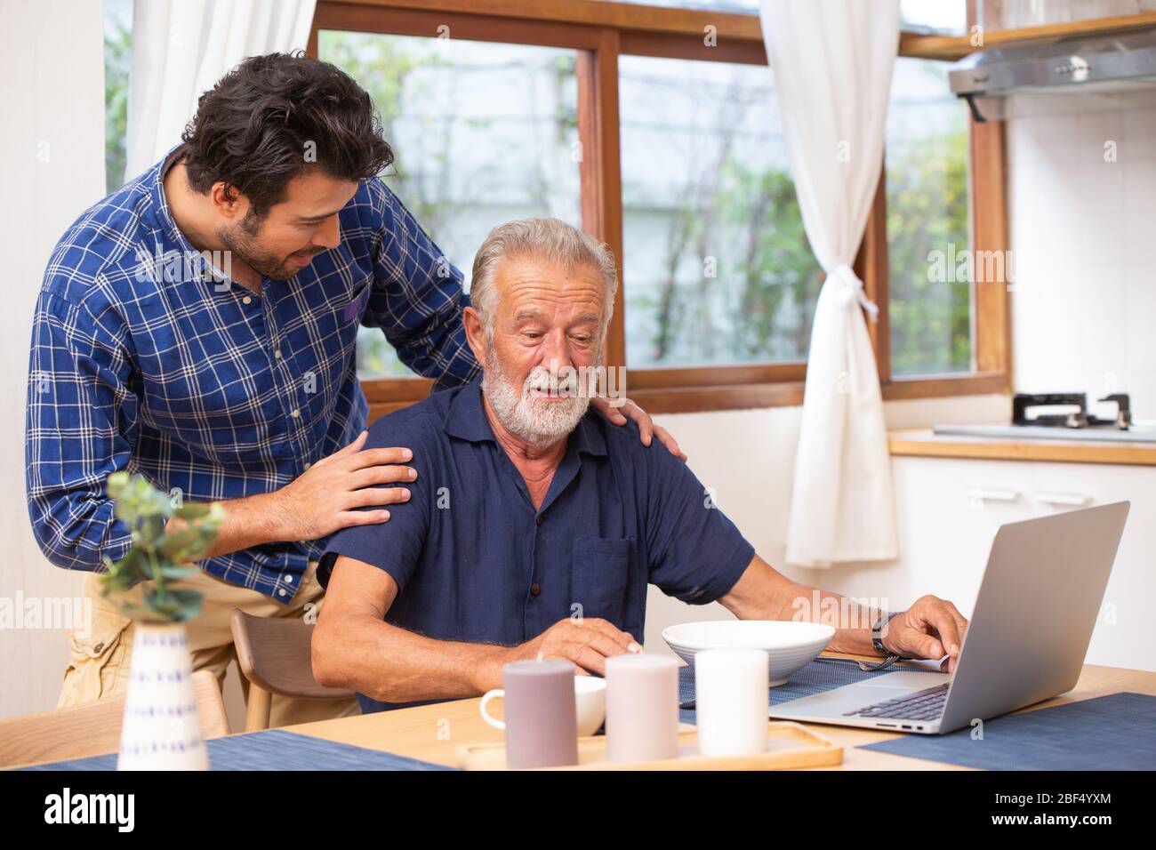 Soins aux aînés à domicile, bon mentor sain vieil homme intelligent utilisant ordinateur portable séjour chez le jeune homme. Banque D'Images