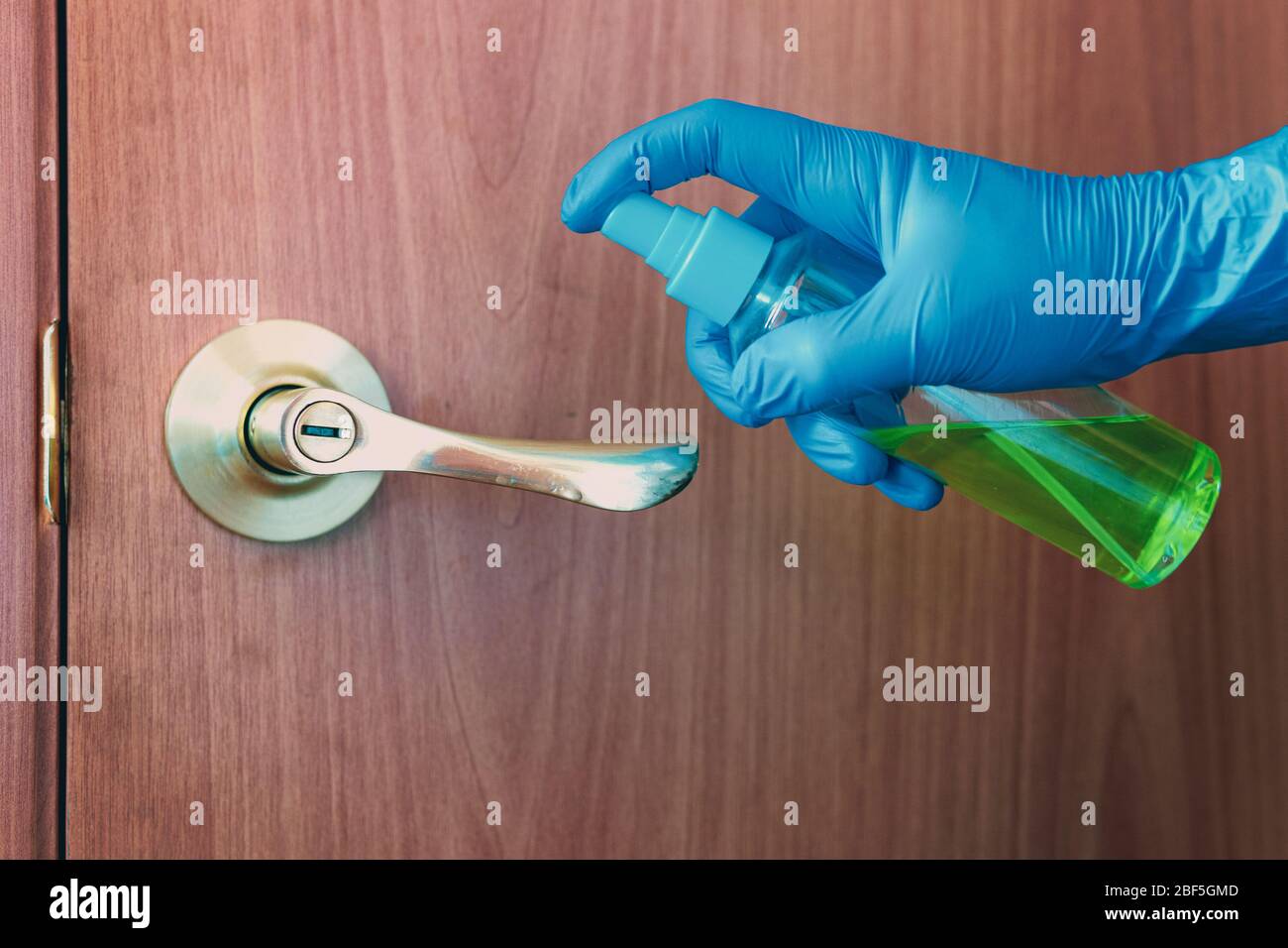 gros plan de la désinfection de la poignée de porte en vaporisant un désinfectant bleu à partir d'une bouteille Banque D'Images