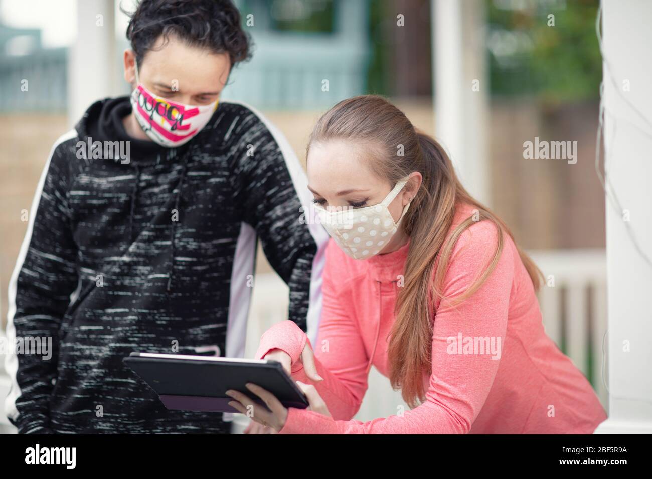 Un jeune homme et une jeune femme regardant un comprimé portant des masques de visage en tissu. La couverture du visage en public est recommandée par CDC dans de nombreux pays pendant à Covid-19 Banque D'Images