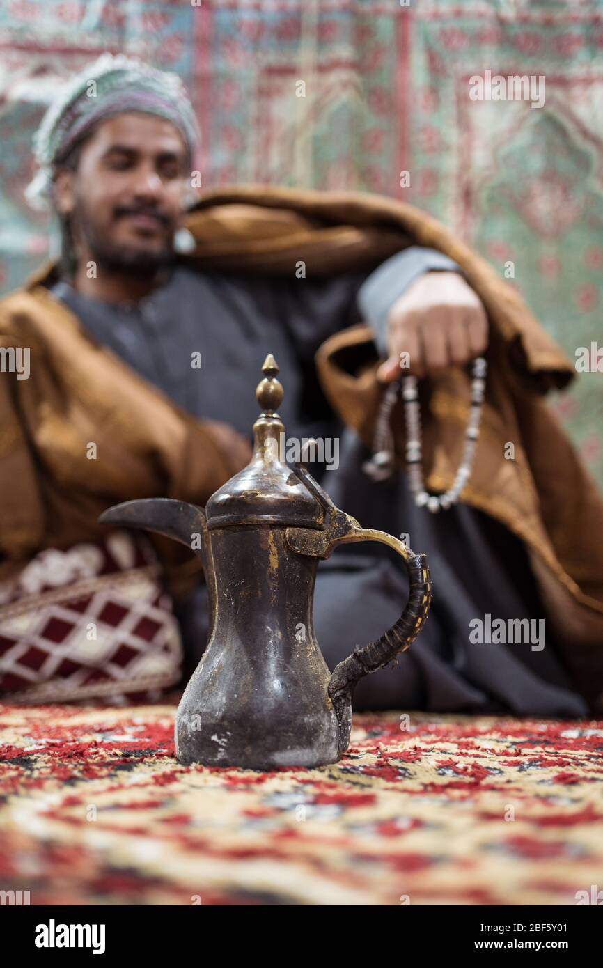 Bédouin homme portant des vêtements traditionnels priant avec une tasbih tout en buvant du thé sur un tapis dans le désert saoudien pendant la nuit, Arabie Saoudite Banque D'Images