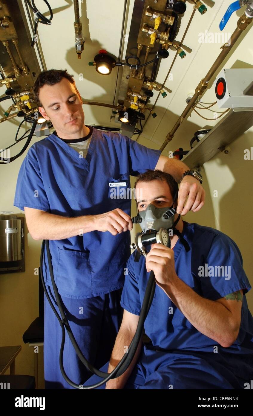 Un technicien médical aide un patient à se cacher avec son masque à oxygène pendant le traitement à l'intérieur de la chambre hyperbare à l'hôpital de St John et St Elilab Banque D'Images