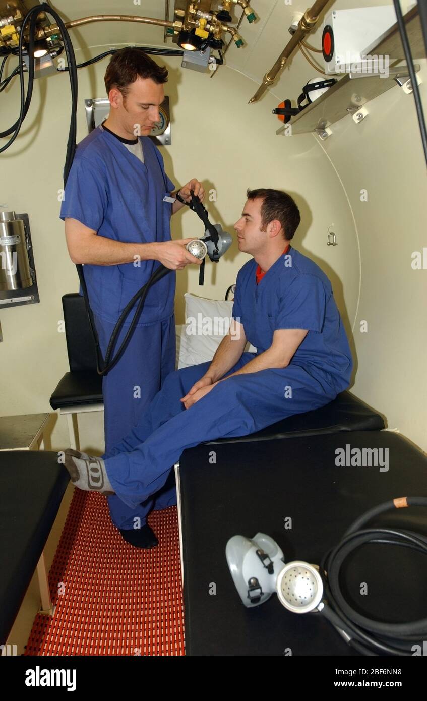 Un technicien médical aide un patient à se cacher avec son masque à oxygène pendant le traitement à l'intérieur de la chambre hyperbare à l'hôpital de St John et St Elilab Banque D'Images