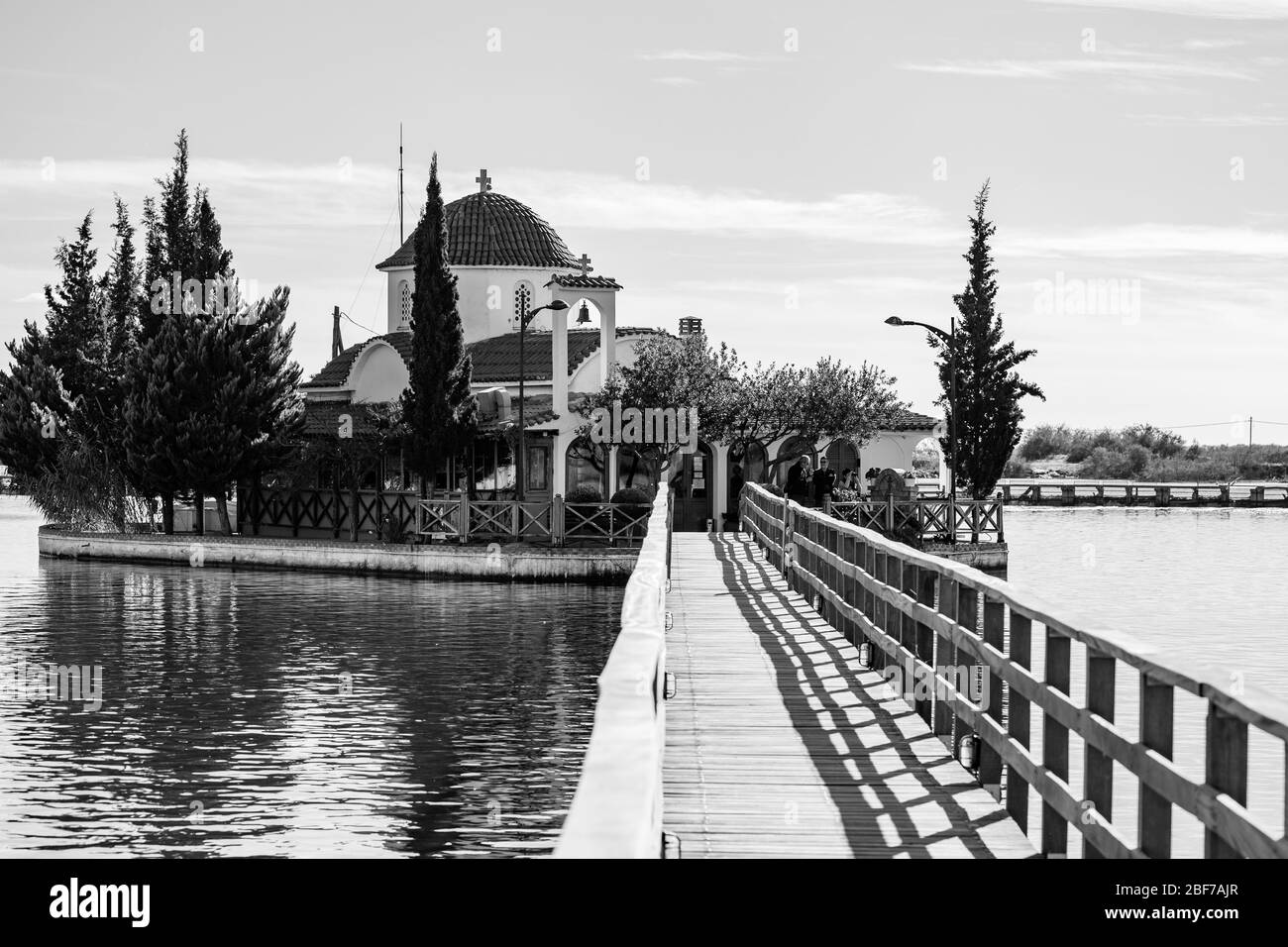 PORTO LAGOS, GRÈCE - 29 NOVEMBRE 2019: Les touristes bénéficient d'un beau monastère de Saint-Nicolas sur le lac de Vistonida, Porto Lagos, région de Xanthi dans le nord de la Grèce, vue noir et blanc avec pont d'eau Banque D'Images