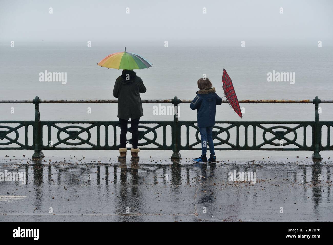Un parent et un enfant avec parasols lors d'une journée de printemps pluvieux à Brighton et Hove front de mer Banque D'Images