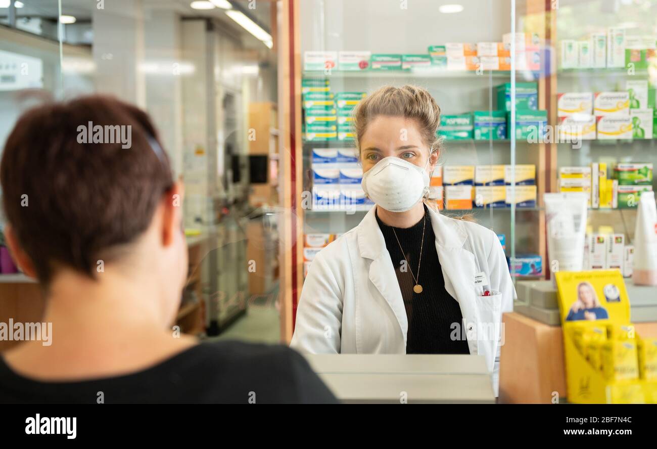 17 avril 2020, Bade-Wuerttemberg, Sulz am Neckar: Laura (r), une employée de pharmacie, porte un porte-bouche alors qu'un client la sert tout en se tenant derrière un écran de Plexiglas. En raison de l'augmentation du nombre de corona à Sulz am Neckar (district de Rottweil), les masques y sont obligatoires depuis le 17.04.2020. Photo: Silas Stein/dpa Banque D'Images