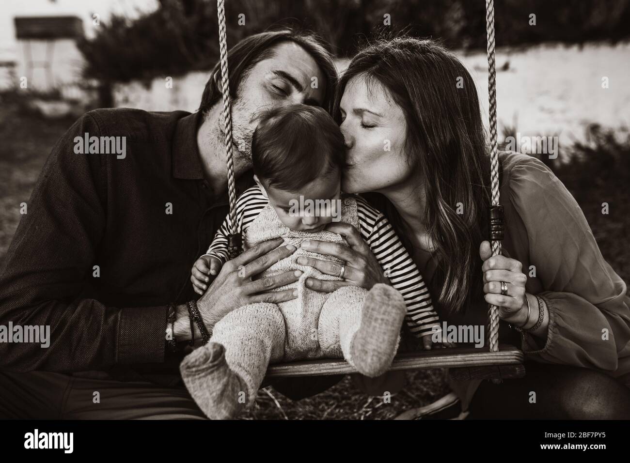 Un Jeune Couple Embrassant Son Bebe Assis Sur Un Balancement Au Jardin En Noir Et Blanc Photo Stock Alamy
