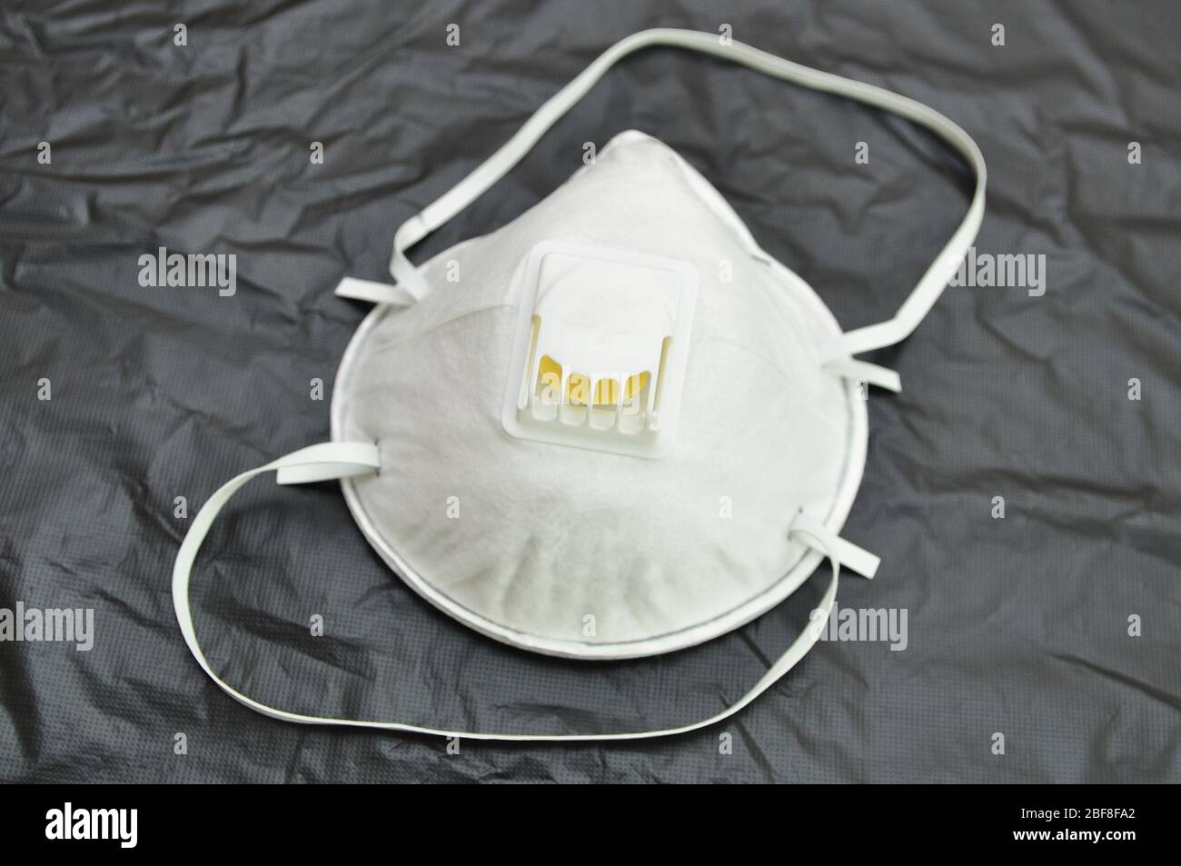 Masque blanc sur fond noir. Respirateur avec valve de ventilation, masque anti-aérosol, efficace pour la protection contre les agents biologiques. Banque D'Images