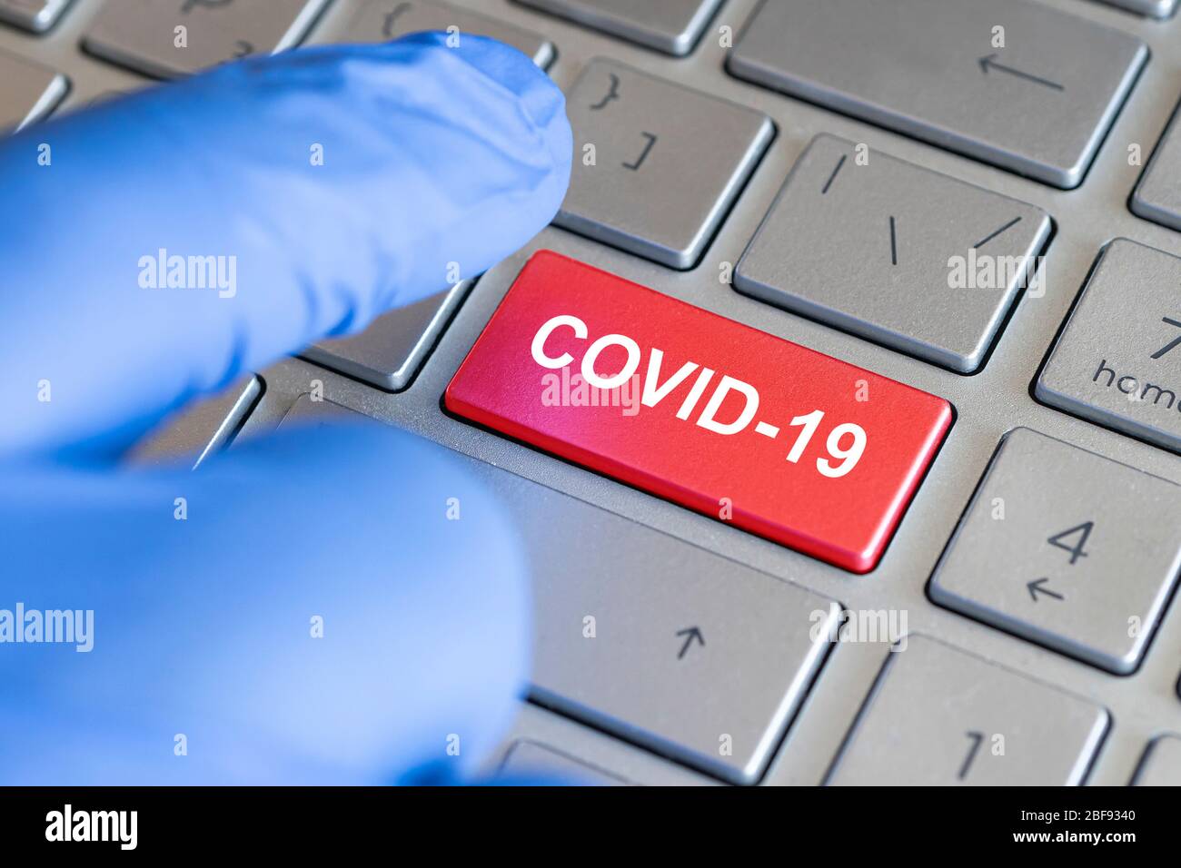 Concept de coronavirus. Clavier avec touche rouge et message COVID-19. Un doigt bleu ganté appuie sur un bouton. Banque D'Images
