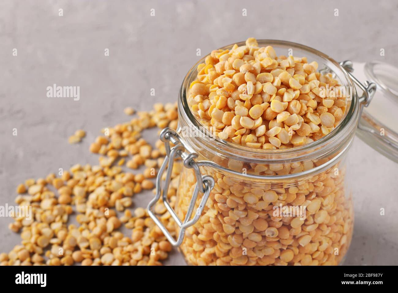 Grains de pois secs dans un bocal en verre sur fond gris, gros plan, espace de copie Banque D'Images