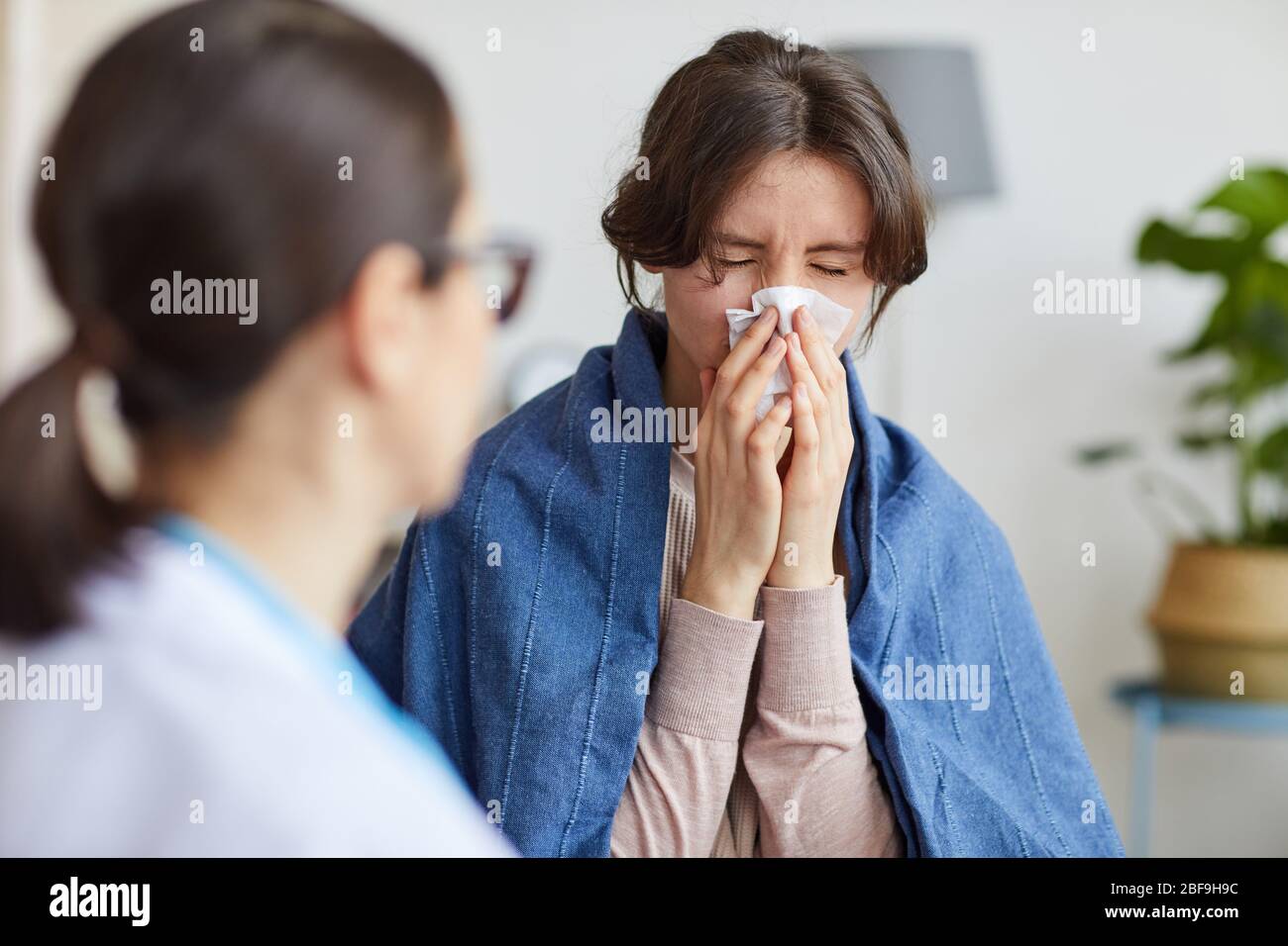 Une femme malade a pris un rhume, elle a le nez et le médecin assis près d'elle et de lui parler à la maison Banque D'Images