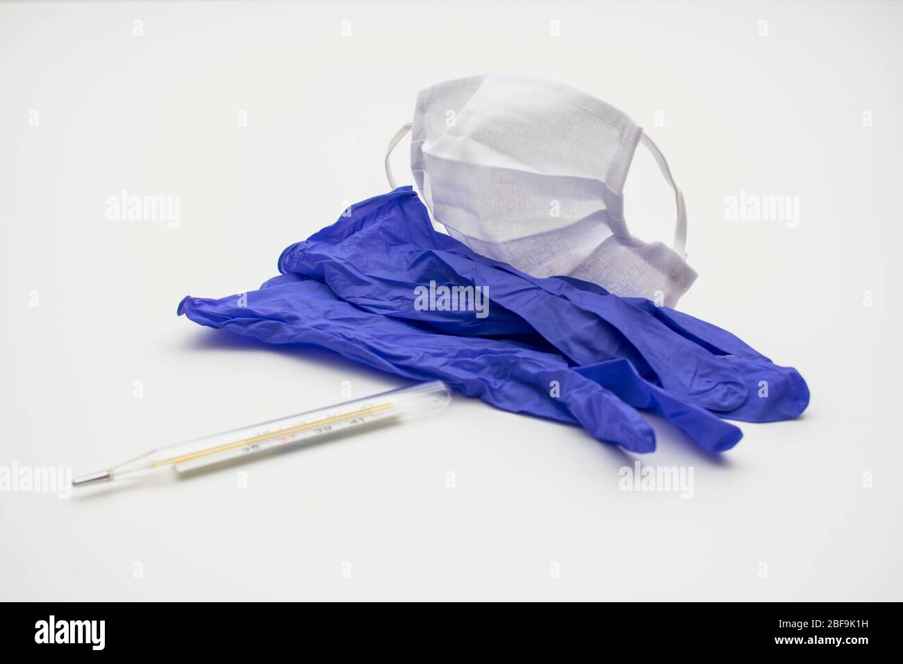 Sur un fond blanc se trouvent des gants chirurgicaux en nitrile, un masque chirurgical et un thermomètre. Banque D'Images