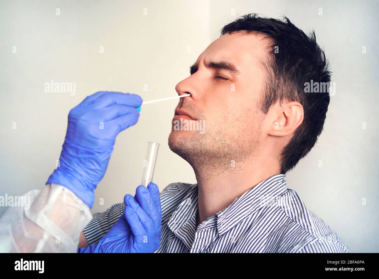 Un médecin en costume protecteur prenant un écouvillon nasal d'une personne pour tester une éventuelle infection à coronavirus. Dépistage des infections virales par le mucus nasal. Banque D'Images