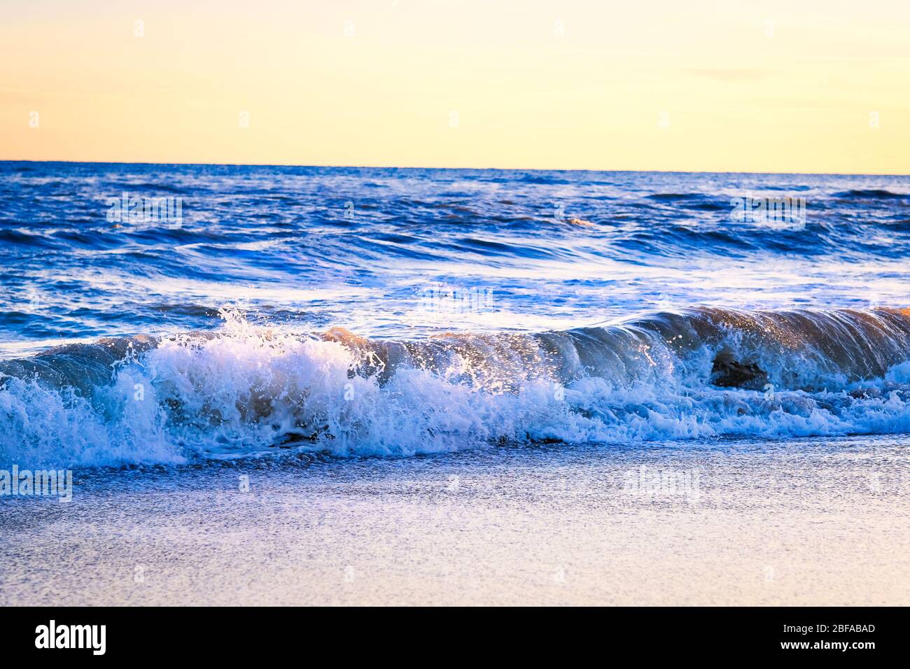 Coucher de soleil sur la plage avec des vagues étincelantes incroyables. Coucher de soleil et vagues sur la plage spectaculaire. Bleu et jaune infini Banque D'Images