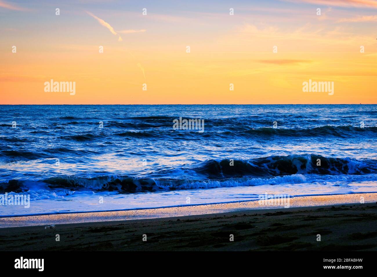 Coucher de soleil sur la plage avec des vagues étincelantes incroyables. Coucher de soleil et vagues sur la plage spectaculaire. Bleu et jaune infini Banque D'Images